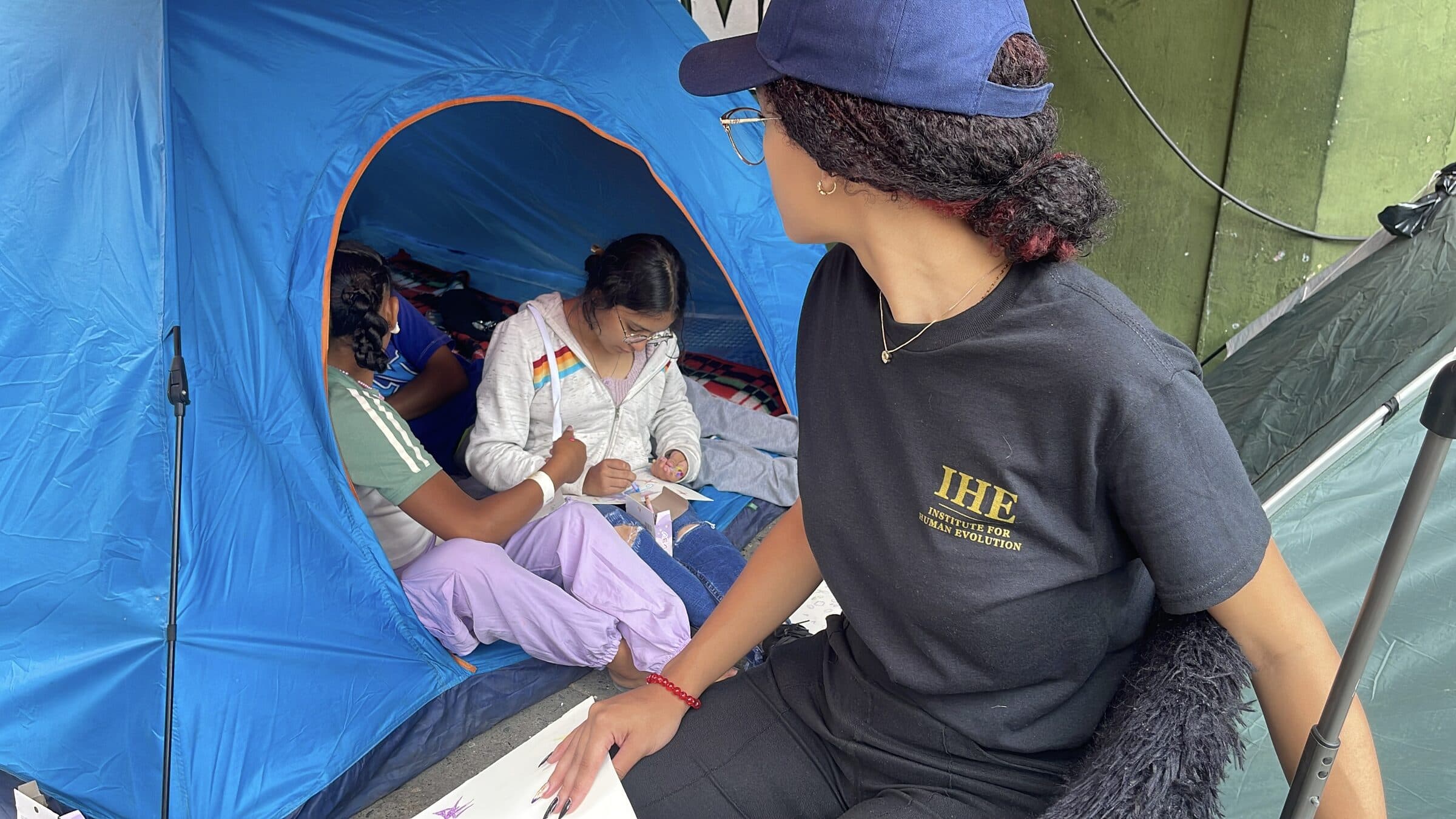 Una adolescente dibuja dentro de una carpa junto a una voluntaria de IHE durante un momento tranquilo del taller de arte.