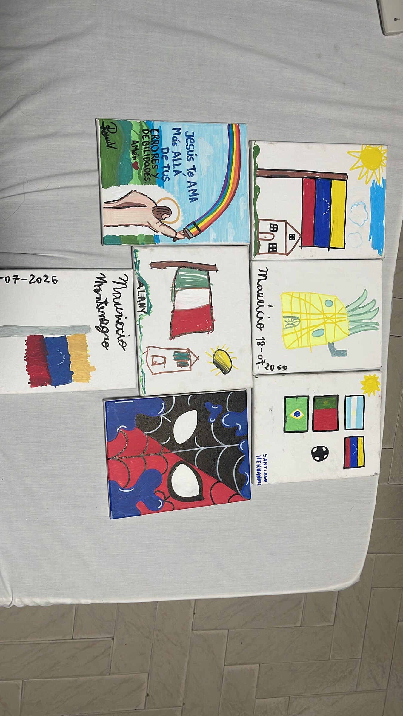 Siete lienzos terminados del taller de arte infantil dispuestos juntos, con banderas, una piña y otros dibujos fechados el 18 de julio de 2026.