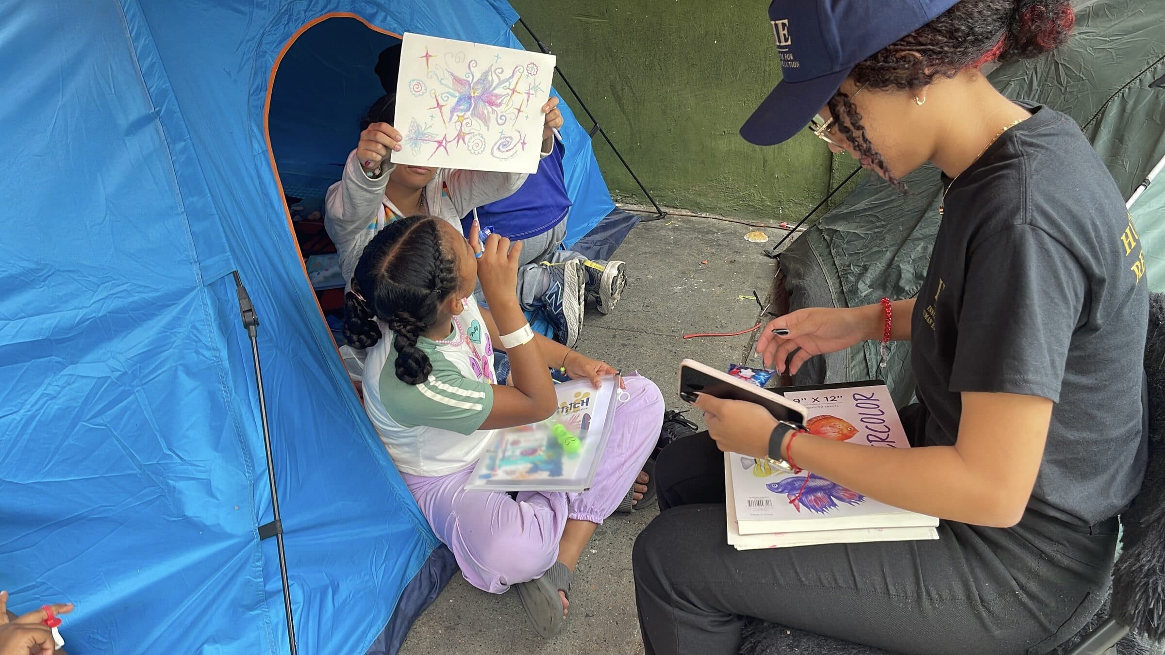 Una niña alza con orgullo su dibujo de una mariposa, que cubre su rostro, durante un taller de arte en el campamento.