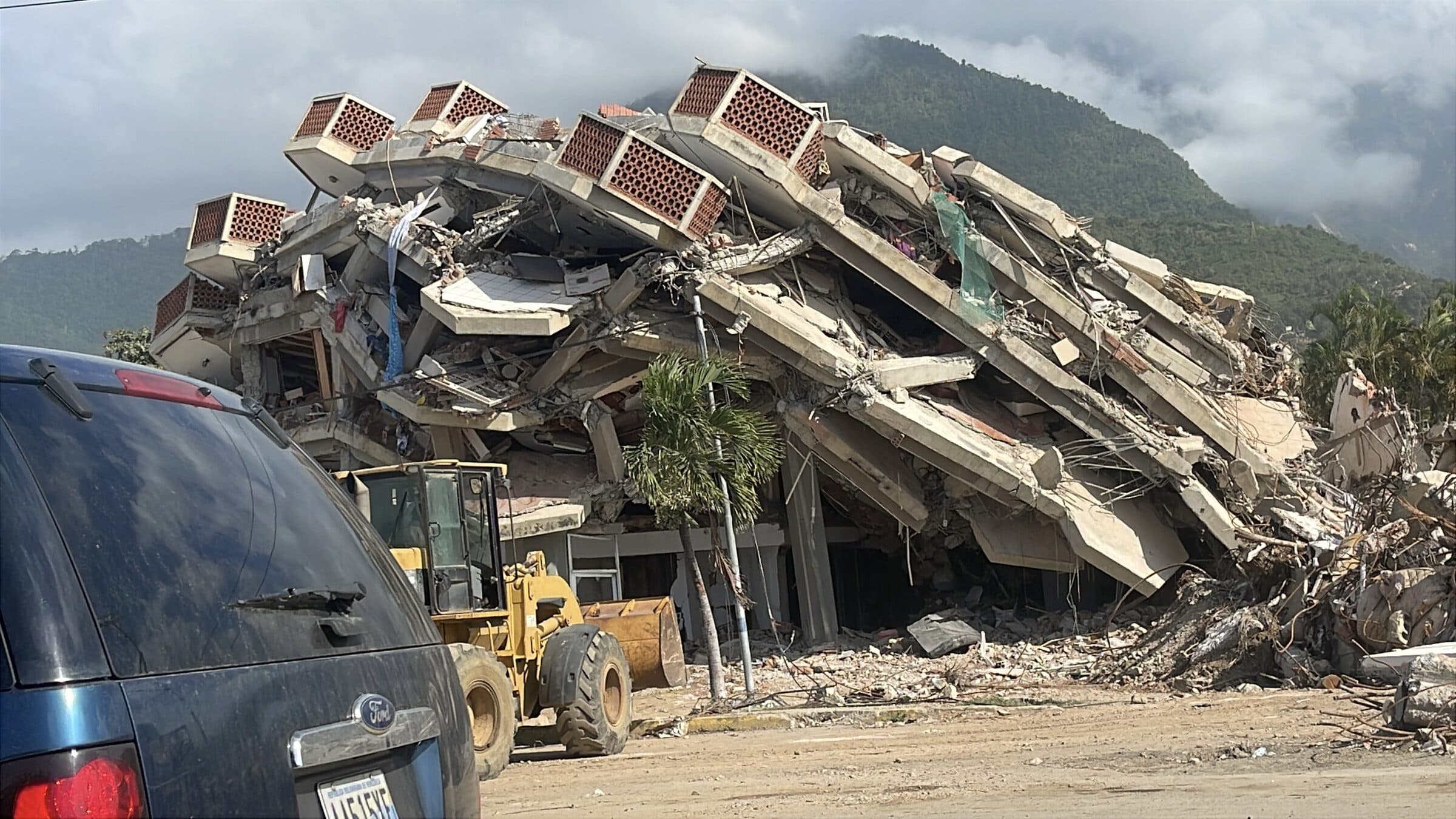 Edificio de varios pisos colapsado por el terremoto en La Guaira, con una cargadora frontal removiendo escombros en su base.