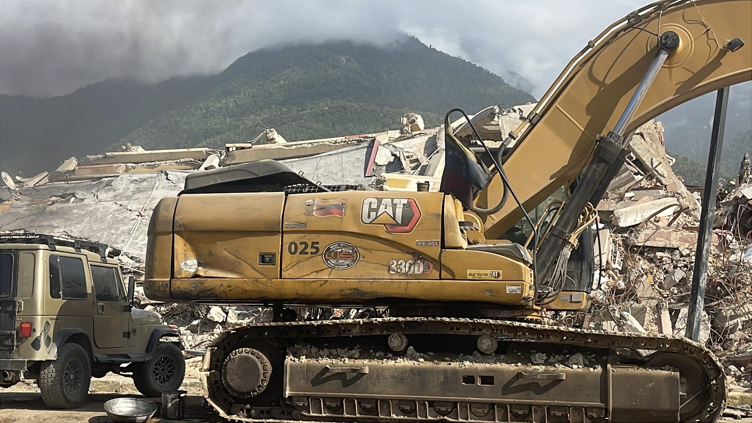 Excavadora CAT con una bandera venezolana durante la remoción de escombros en edificios colapsados en La Guaira.