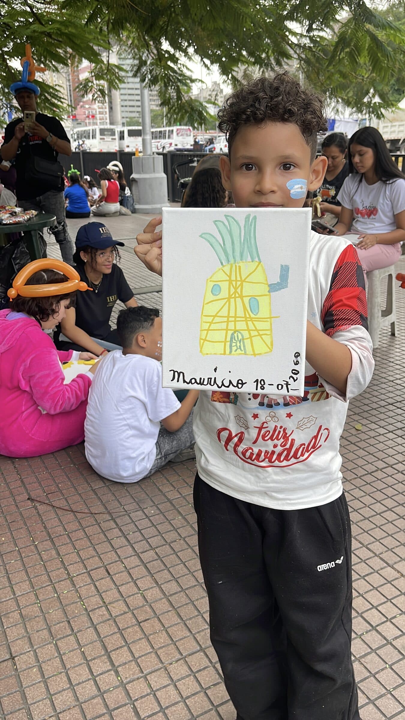 Un niño sostiene con orgullo su pintura de una piña durante el taller de arte de IHE.