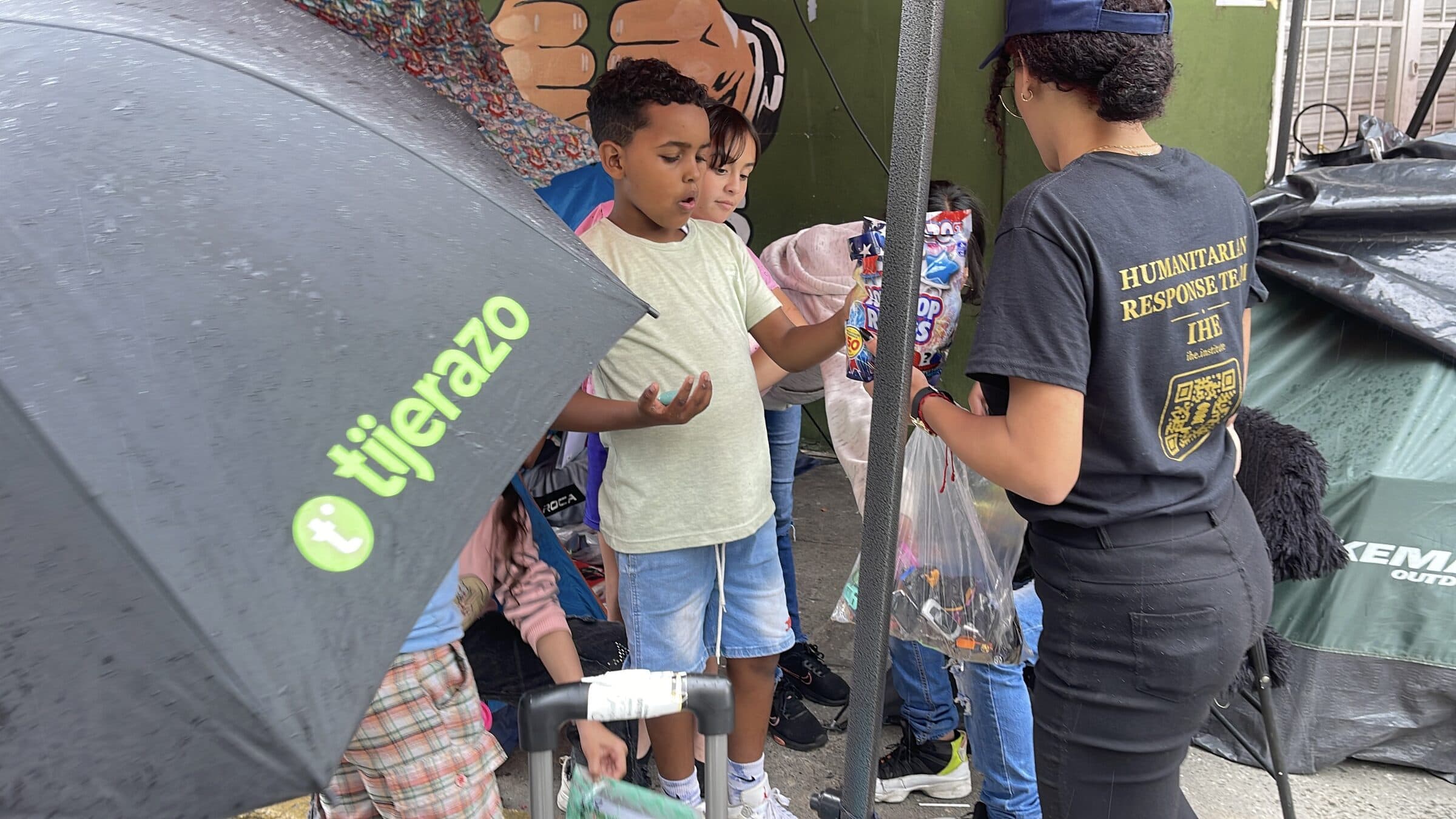 Un niño recibe juguetes y dulces con ambas manos durante una entrega de IHE en el campamento.
