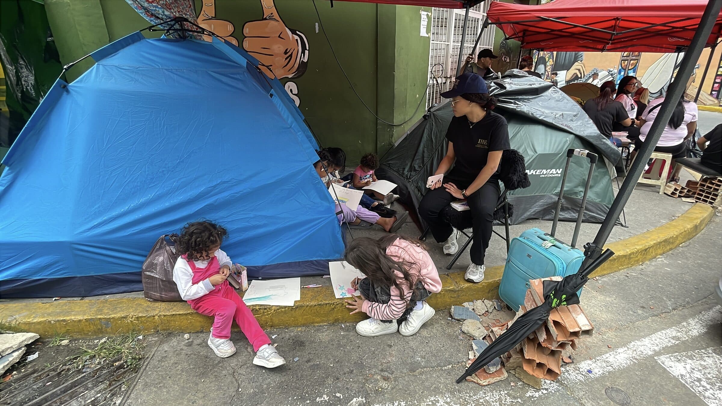 Niños dibujan con crayones en la acera junto a las carpas del campamento Ojitos de Chávez durante un taller de arte de IHE.