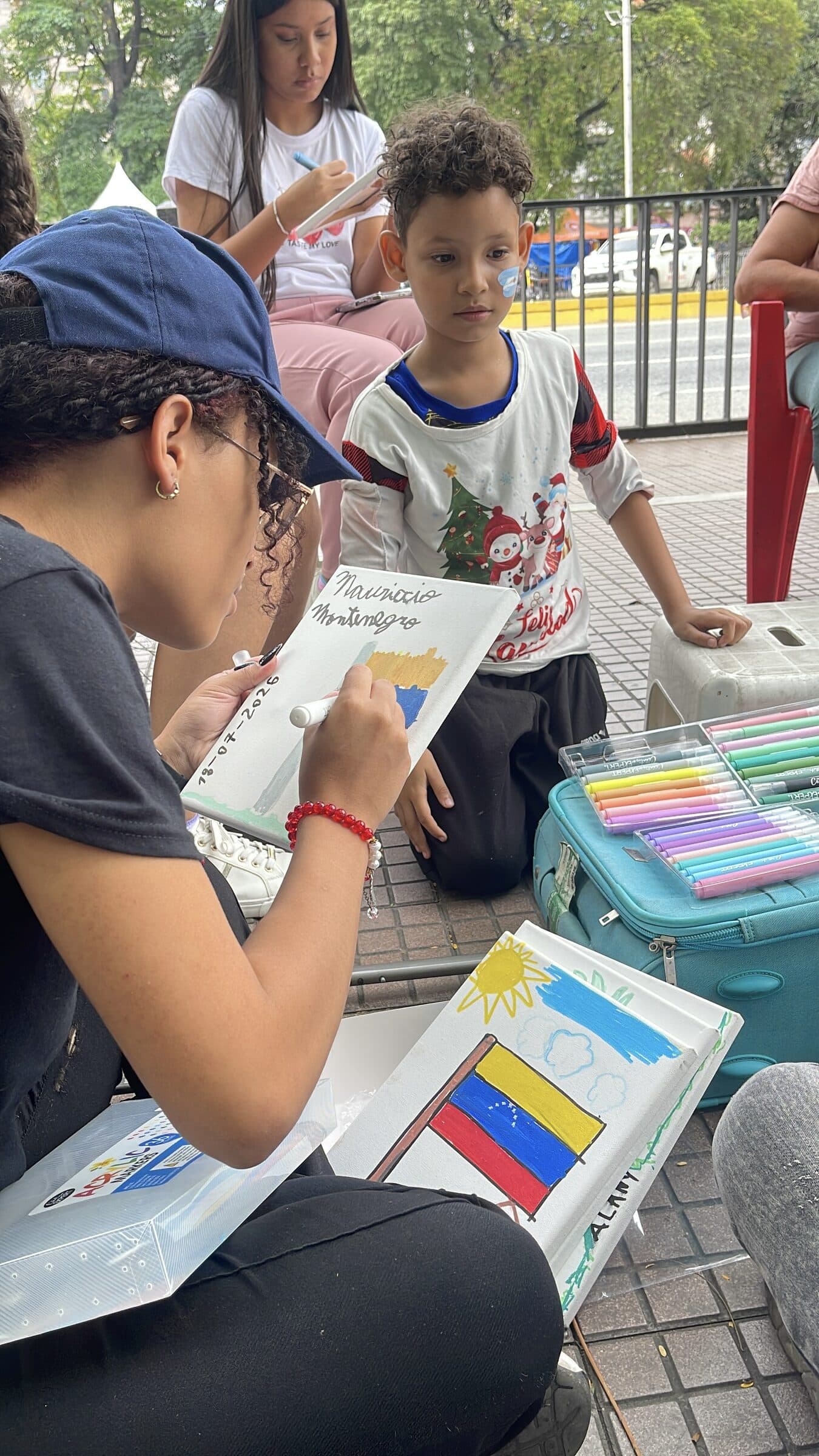 Una voluntaria de IHE firma un lienzo terminado mientras el pequeño artista observa de cerca.