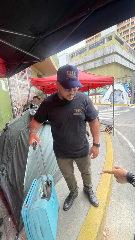 Juan kneeling beside a rolling suitcase, unpacking relief supplies near a tent.
