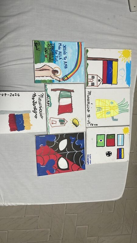 A collection of children's drawings laid out on a table, including a Venezuelan flag and a house.