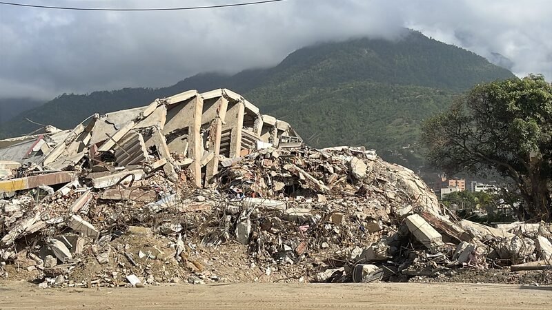 Pile of concrete rubble from a collapsed multi-story building, with mountains in the background.