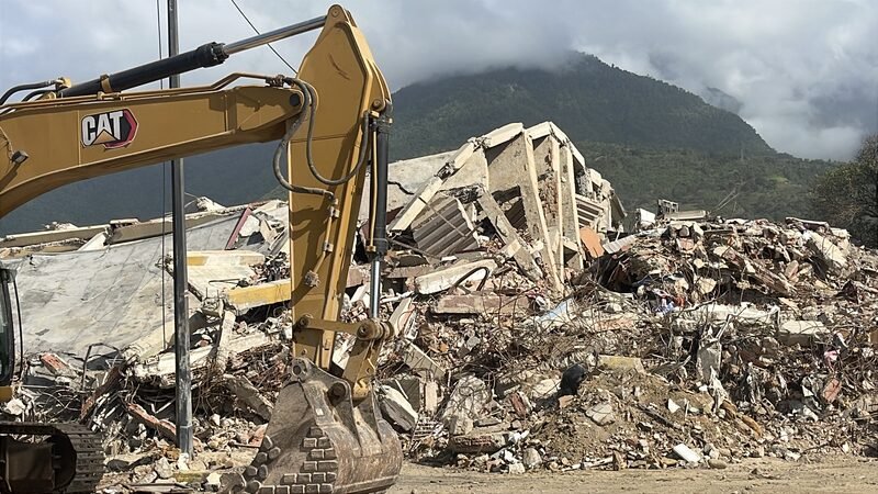 An excavator working on a pile of concrete rubble from a collapsed building.