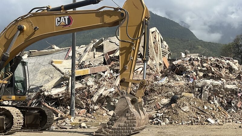 An excavator working on a pile of concrete rubble from a collapsed building.