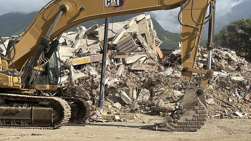 An excavator working on a pile of concrete rubble from a collapsed building.