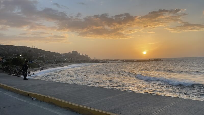 Sun setting over the ocean along a coastal road.