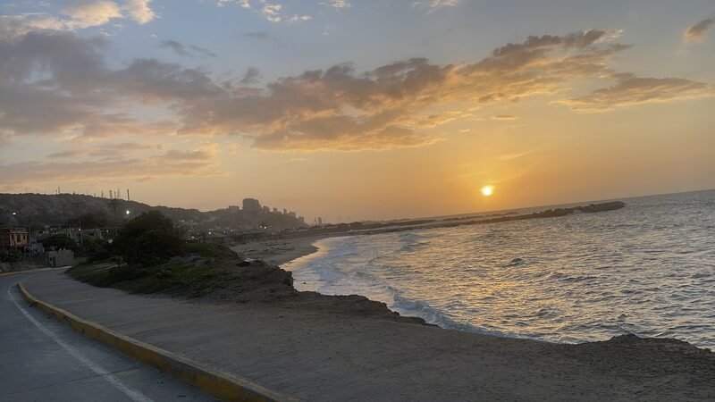 Sun setting over the ocean along a coastal road.