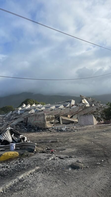 Pile of concrete rubble from a collapsed multi-story building, with mountains in the background.