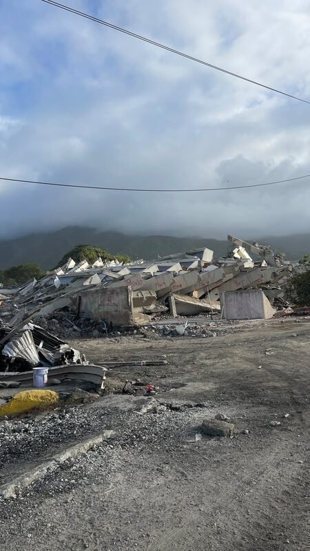 Pile of concrete rubble from a collapsed multi-story building, with mountains in the background.