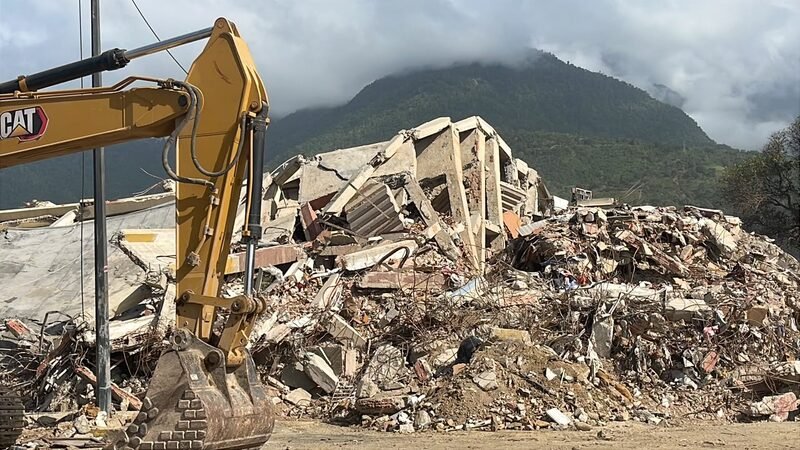 An excavator working on a pile of concrete rubble from a collapsed building.
