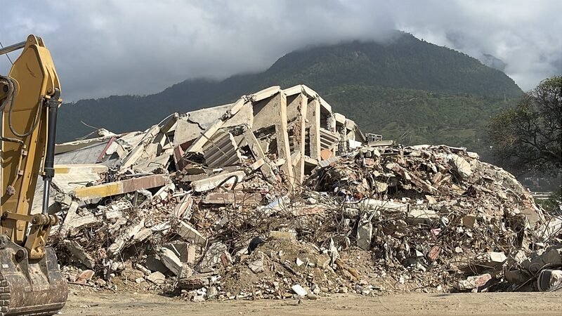 An excavator working on a pile of concrete rubble from a collapsed building.