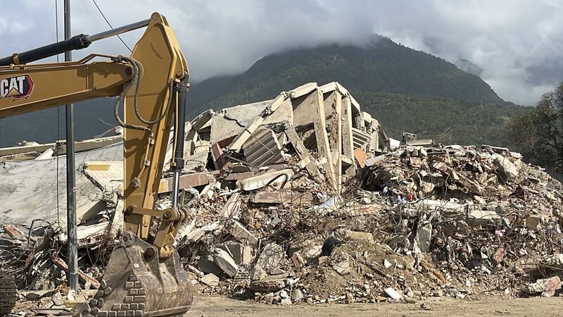 An excavator working on a pile of concrete rubble from a collapsed building.