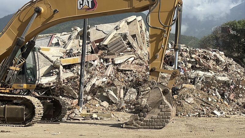 An excavator working on a pile of concrete rubble from a collapsed building.