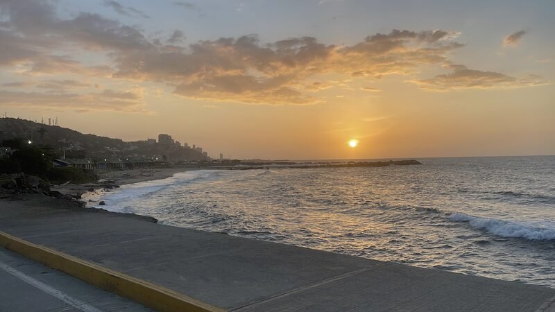Sun setting over the ocean along a coastal road.