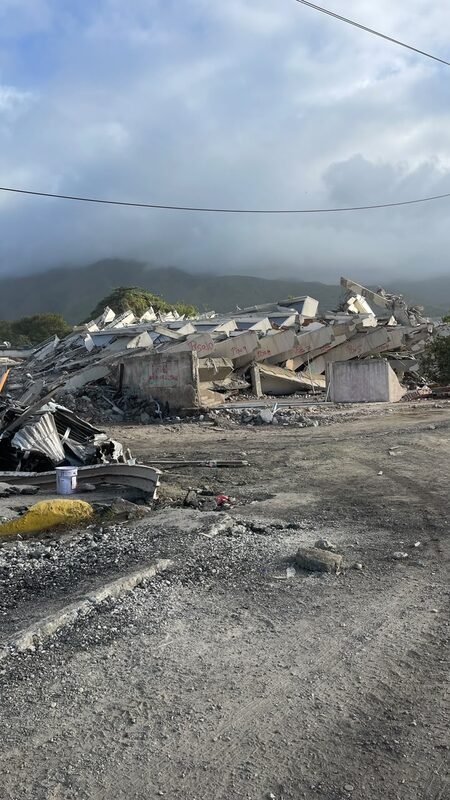 Concrete rubble and debris piled along a roadside, mountains in the background.
