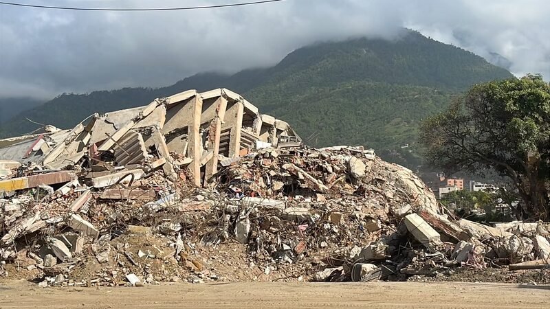 Concrete rubble and debris piled along a roadside, mountains in the background.