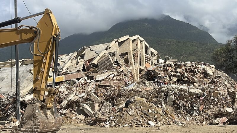 An excavator working on a pile of concrete rubble from a collapsed building.