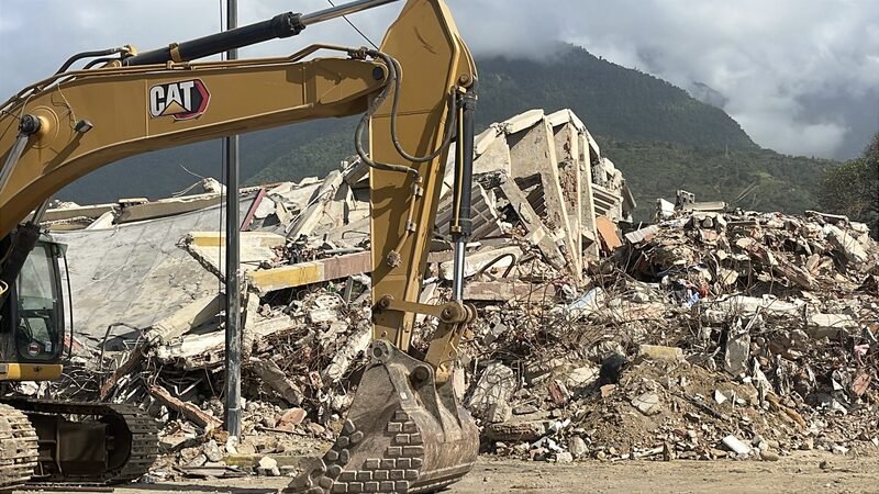 An excavator working on a pile of concrete rubble from a collapsed building.