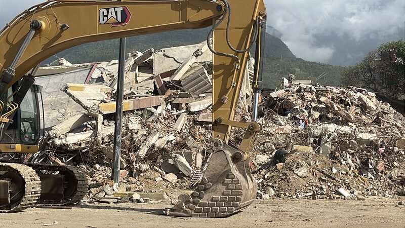 An excavator working on a pile of concrete rubble from a collapsed building.