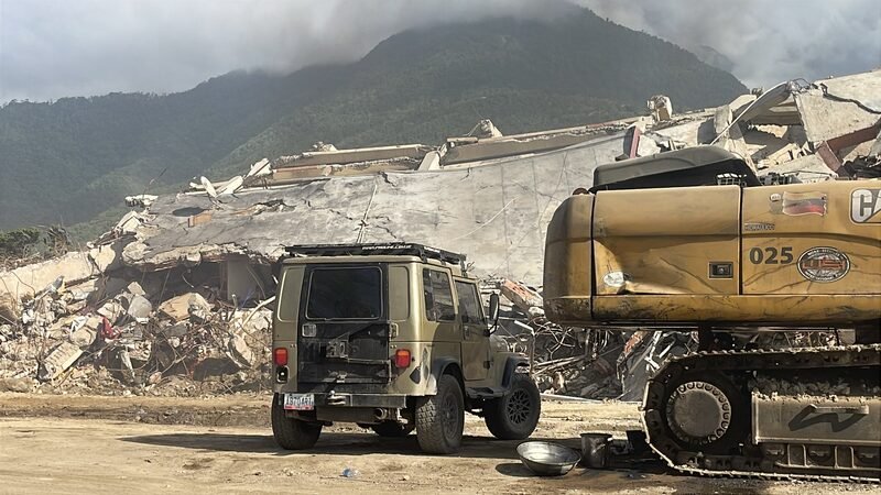 An excavator working on a pile of concrete rubble from a collapsed building.
