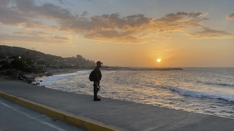 Sun setting over the ocean along a coastal road.